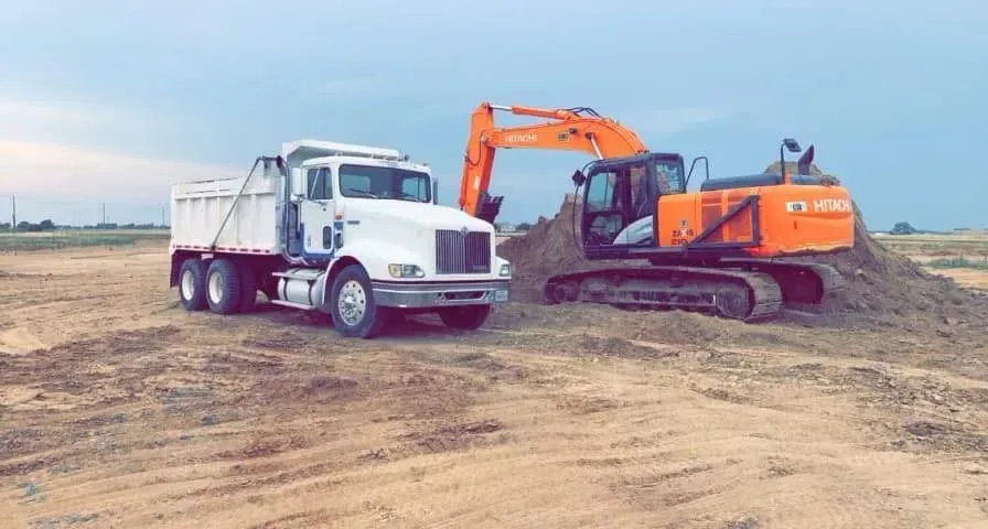 White dump truck and orange excavator working on a dirt construction site under a clear sky
