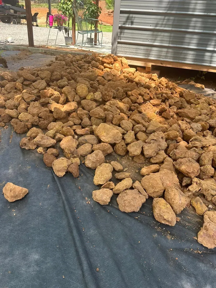 Large pile of brown rocks on a black tarp beside a building outdoors