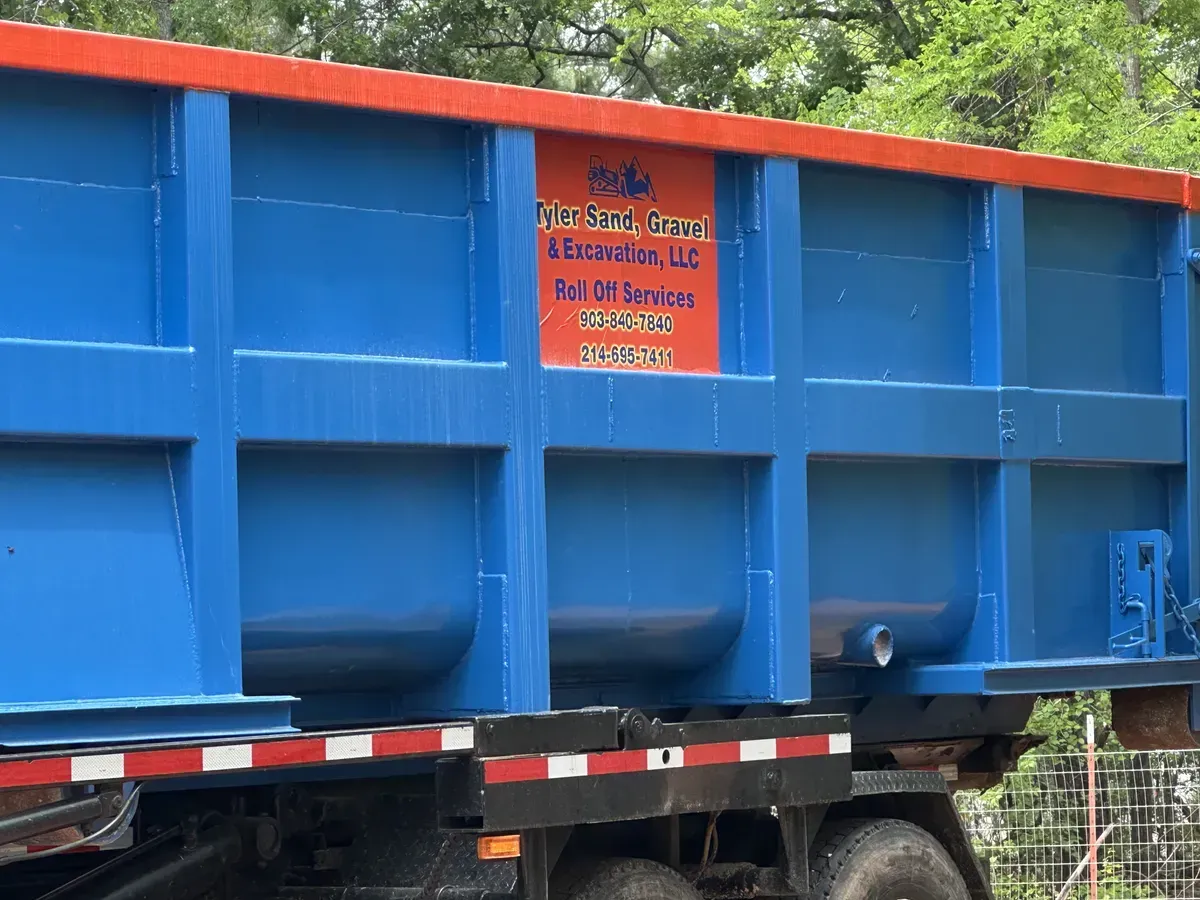 Blue industrial dump truck trailer with orange safety sign on the side, parked outdoors among trees