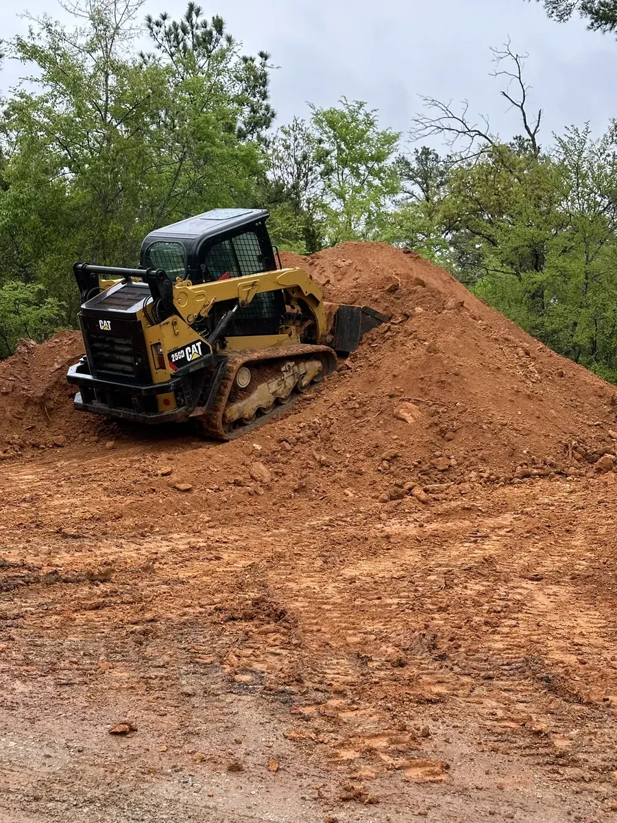 Yellow bulldozer pushing a dirt pile at a muddy construction site with trees in the background