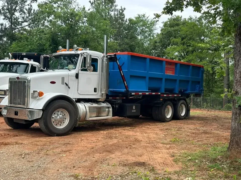 White dump truck with blue bed parked on a dirt lot near trees