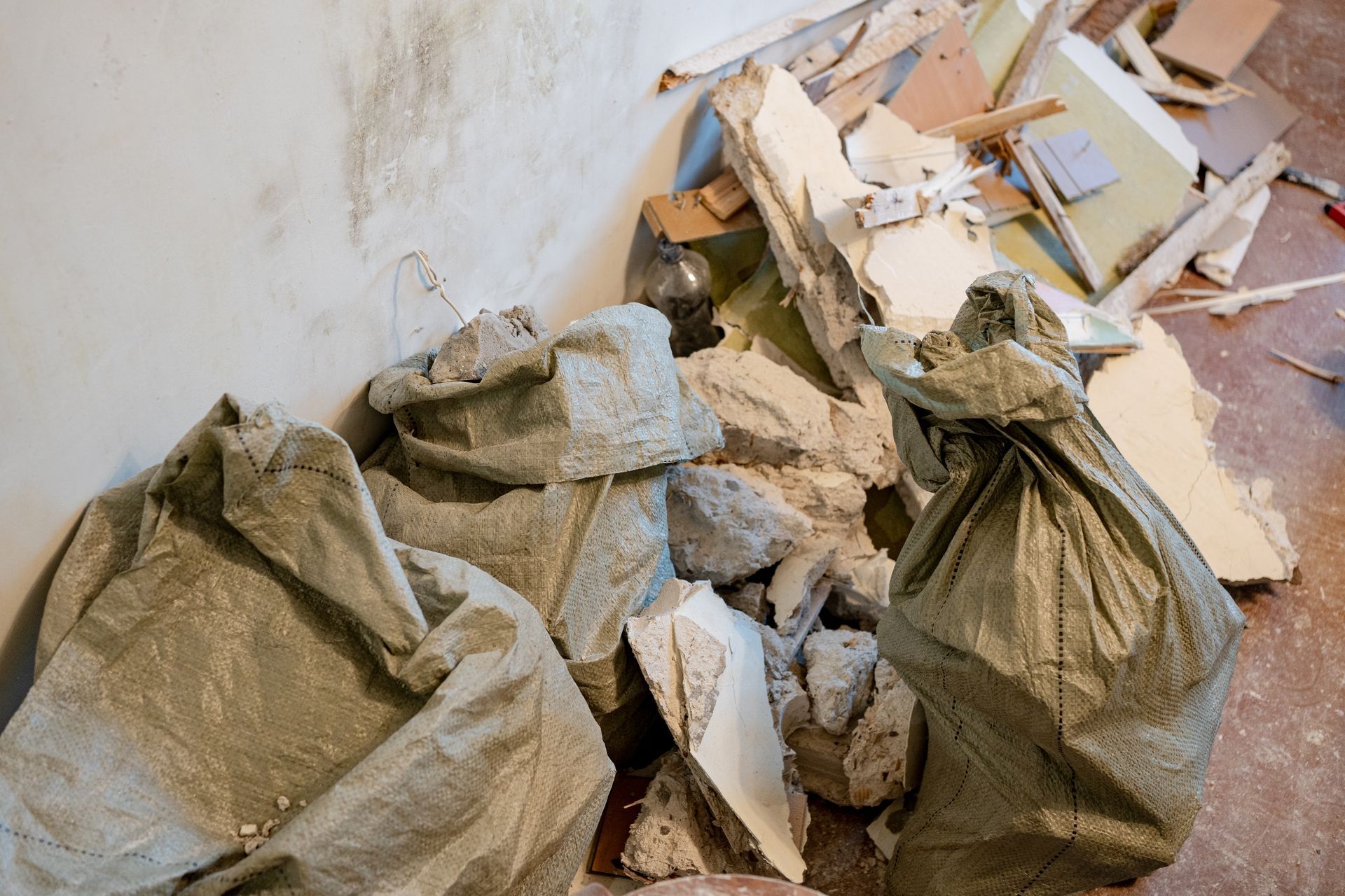 Piles of broken drywall and debris in trash bags beside a wall during cleanup work