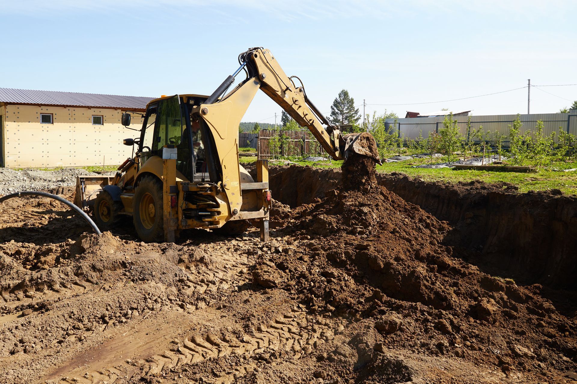 Yellow backhoe digging soil at a construction site beside a large trench