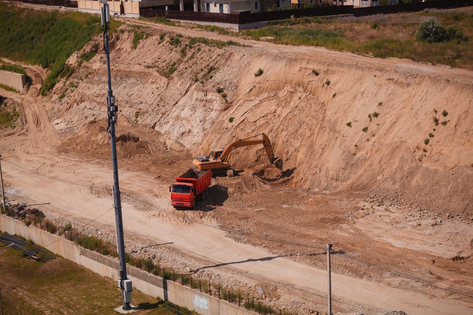 Excavator and red dump truck working on a dirt hillside construction site