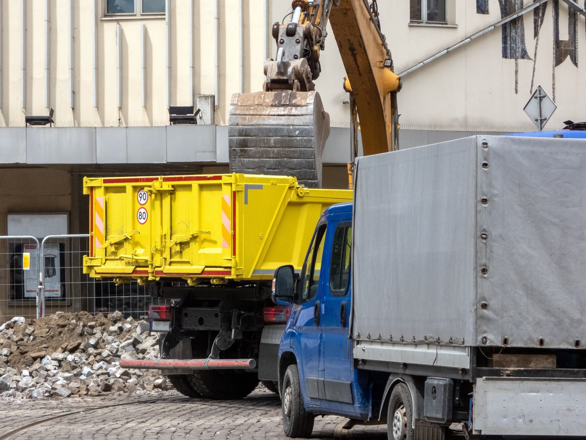 Blue truck and yellow dump trailer at a construction site with an excavator loading rubble