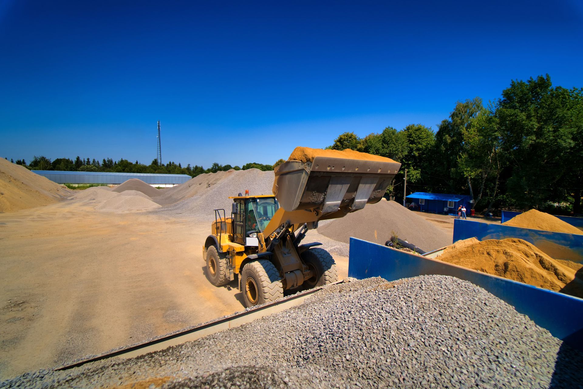 Front loader dumping gravel in a bright outdoor quarry under a blue sky