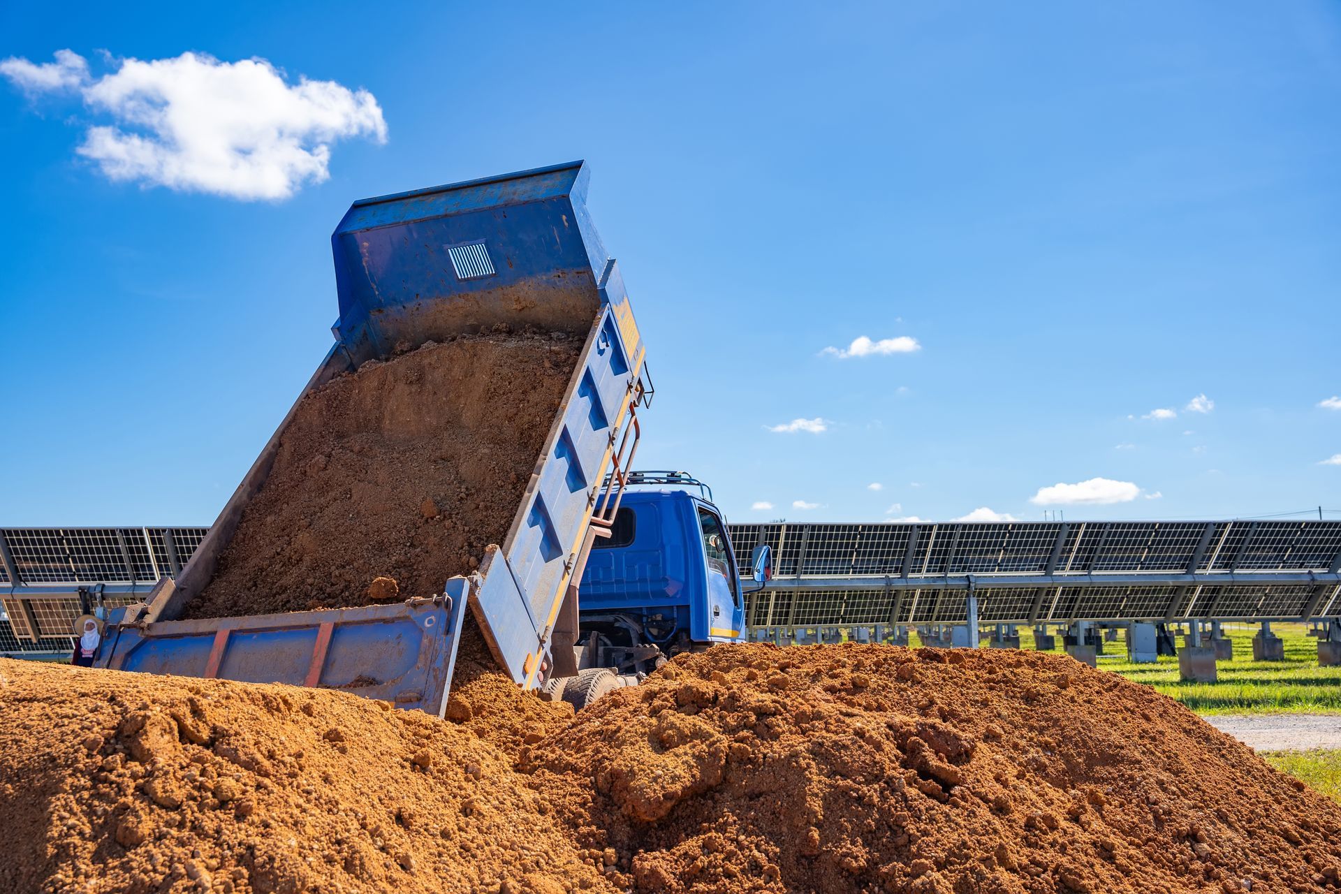 Blue dump truck unloading soil at a farm under a clear sky