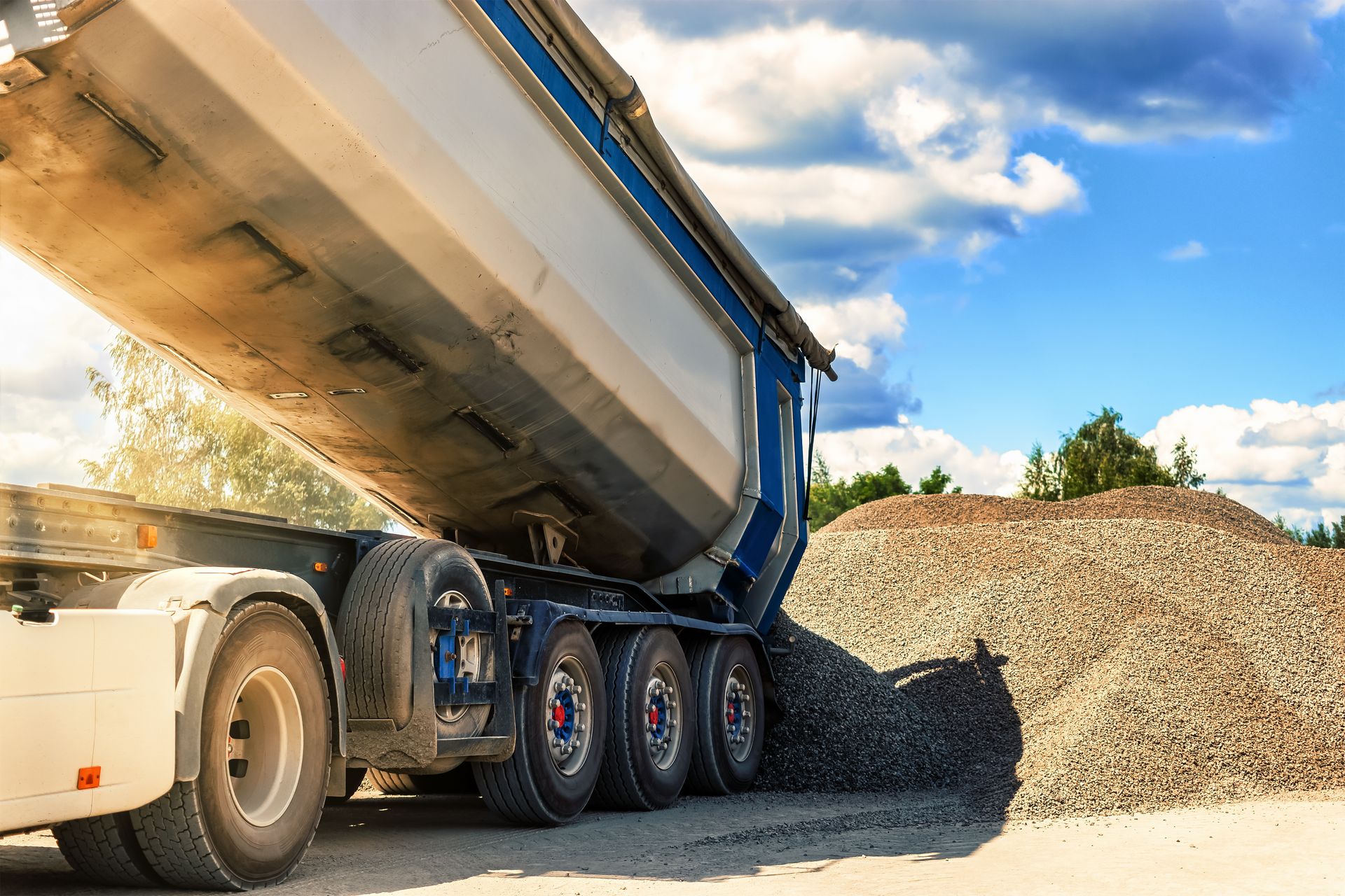 Dump truck unloading gravel at a construction site under a sunny sky