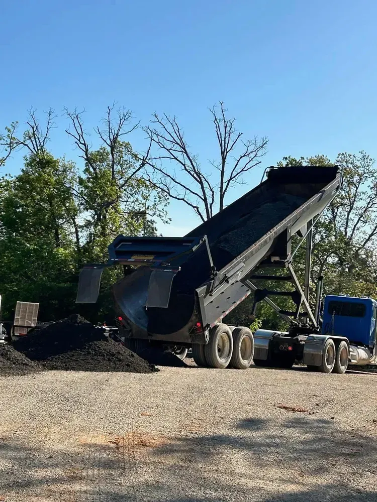 Dump truck unloading gravel at a construction site under a clear blue sky