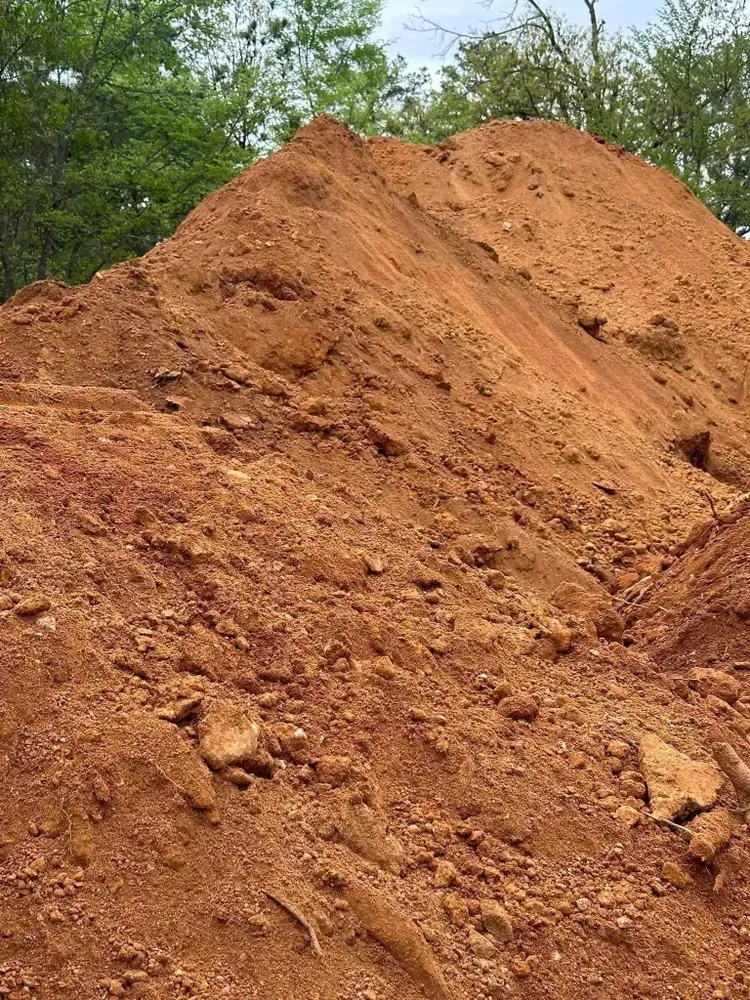 Large mound of reddish-brown dirt with green trees in the background