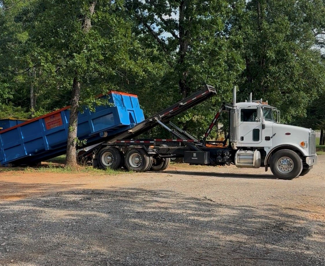 Dump truck unloading sand beside green trees
