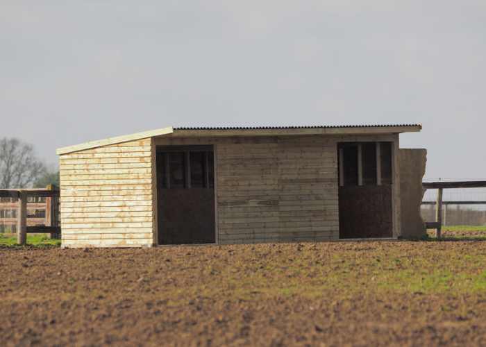 A small wooden shed is sitting in the middle of a field.