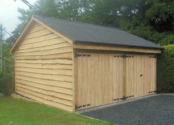A wooden garage with a black roof is sitting on top of a gravel driveway.