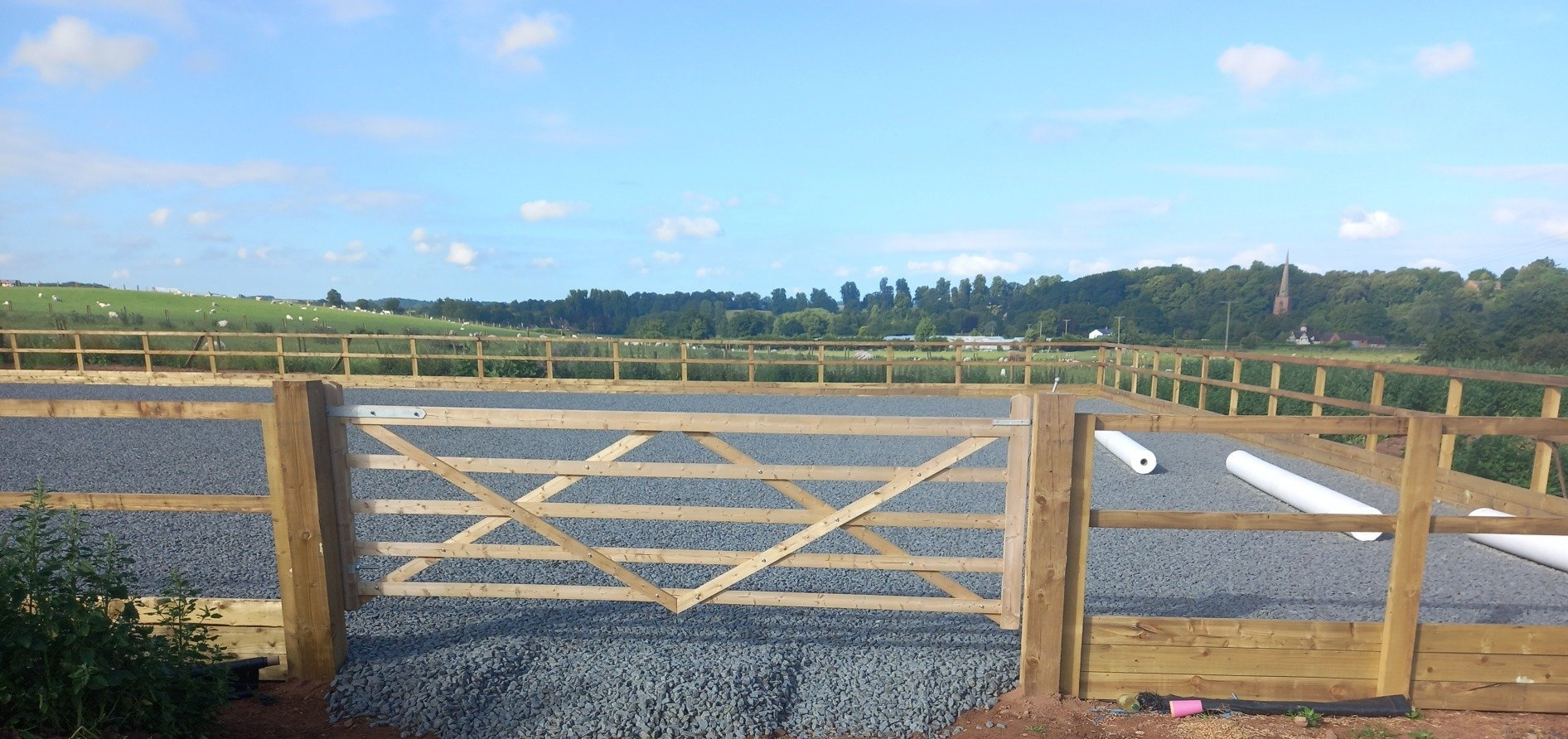 A wooden fence with a gate in the middle of a gravel road.