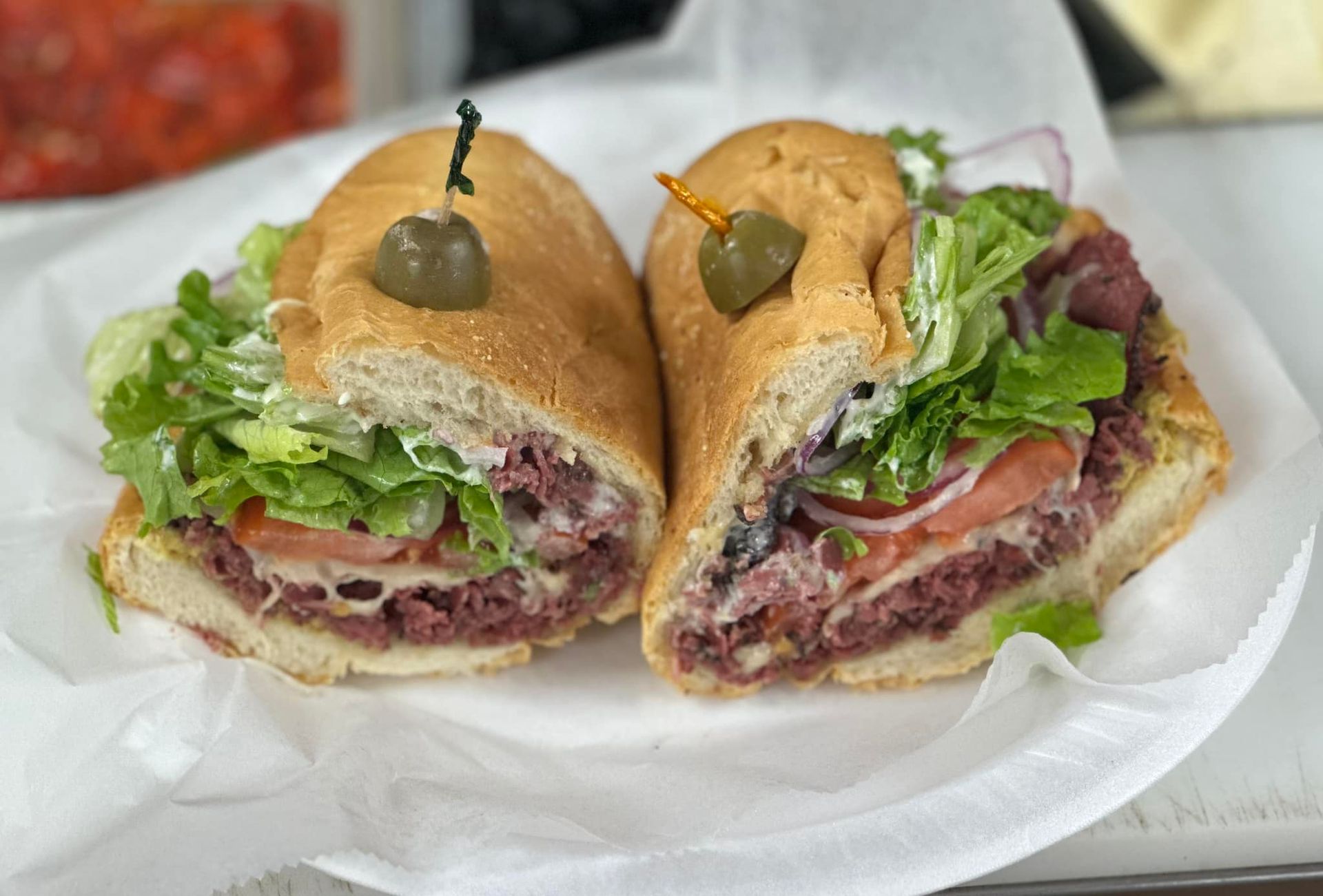 Two sub sandwiches are cut in half on a paper plate.