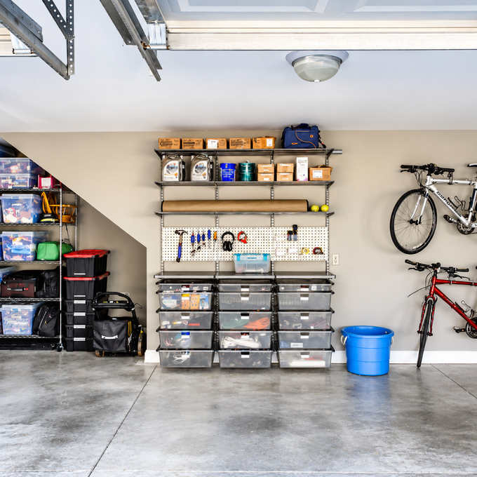 Garage wall with organized storage shelves, bins, tools, bicycles, and a blue bucket on the floor