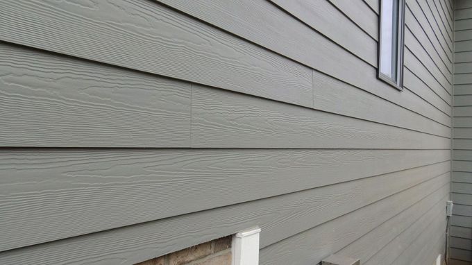 Close-up of gray house siding with horizontal panels and a small window at the right edge