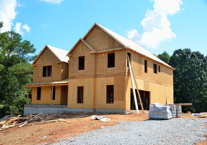 Unfinished two-story brick house under construction with scaffolding on a dirt lot and blue sky