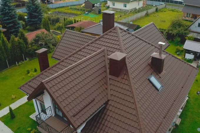 Aerial view of a brown-roofed house with chimneys in a suburban neighborhood.