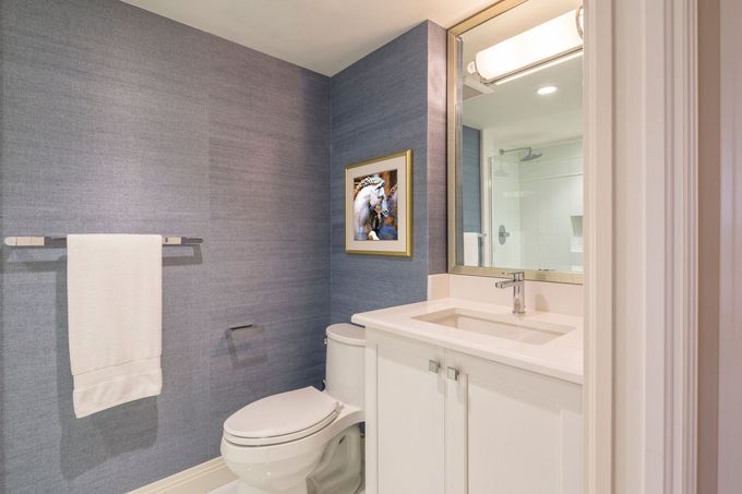 Small bathroom with toilet, sink, towel, and framed artwork on blue-gray walls.