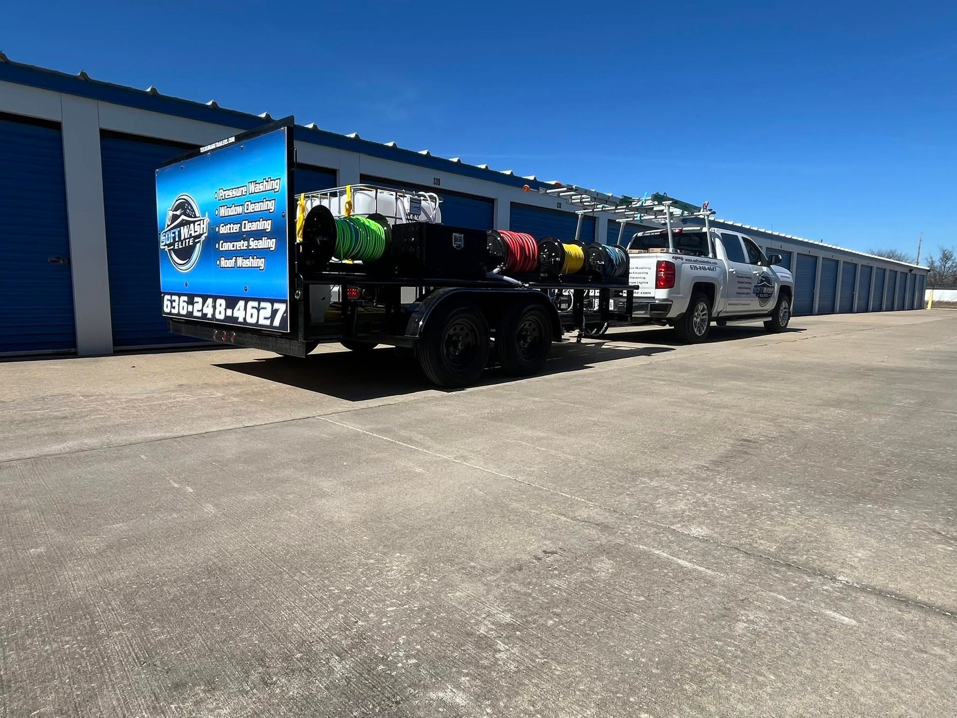 Truck and trailer parked beside blue storage units under a clear sky