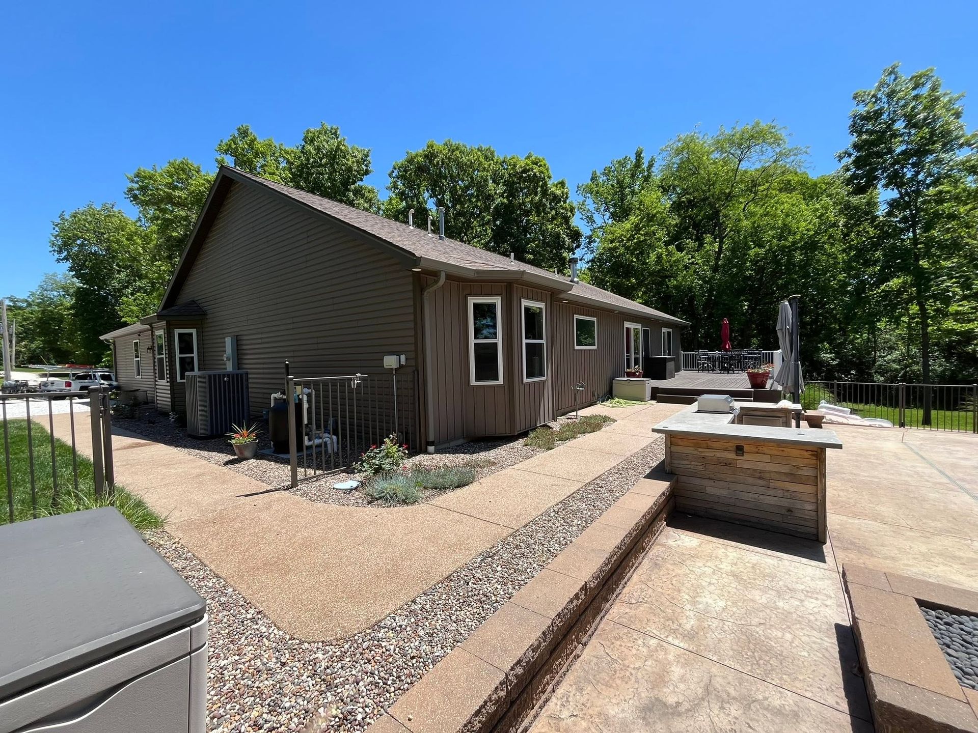 Brown house with gravel courtyard, ramp, and patio under a bright blue sky