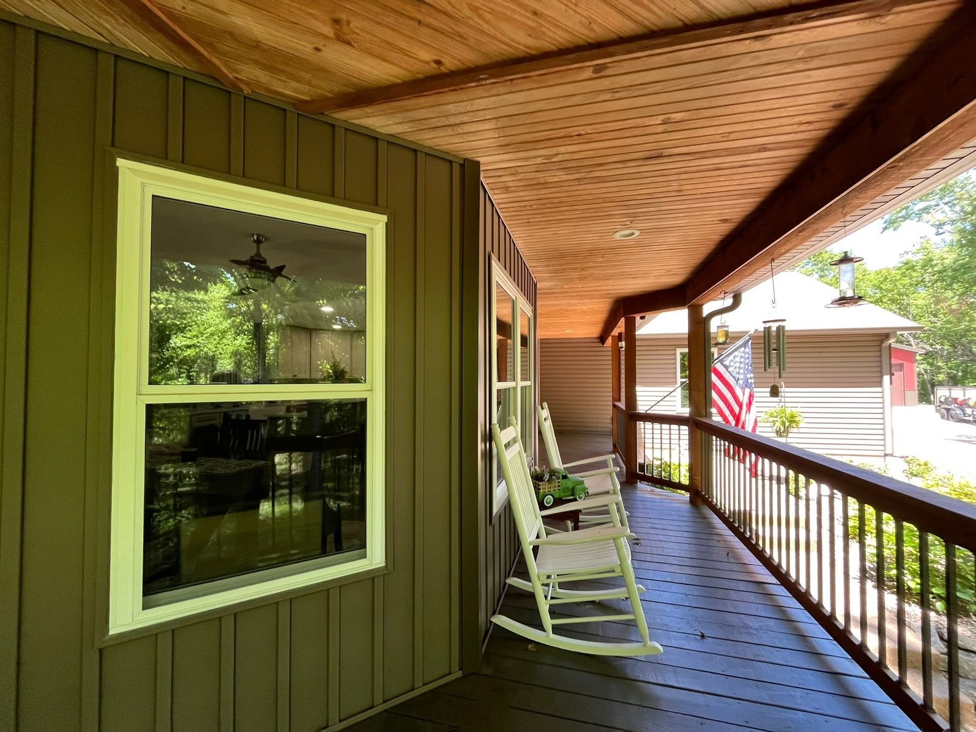 Covered porch with green siding, wood ceiling, rocking chairs, and a railing overlooking the yard.