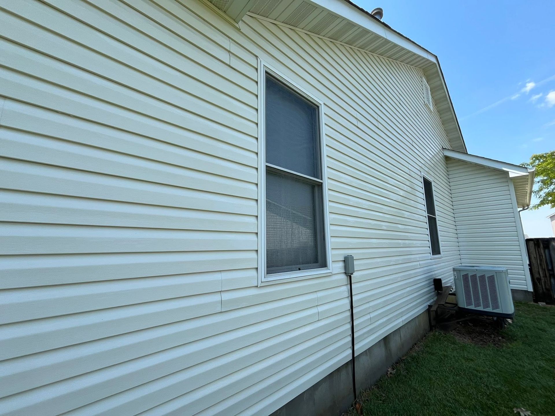 White vinyl house siding with a window, downspout, and outdoor HVAC unit beside a grassy yard.