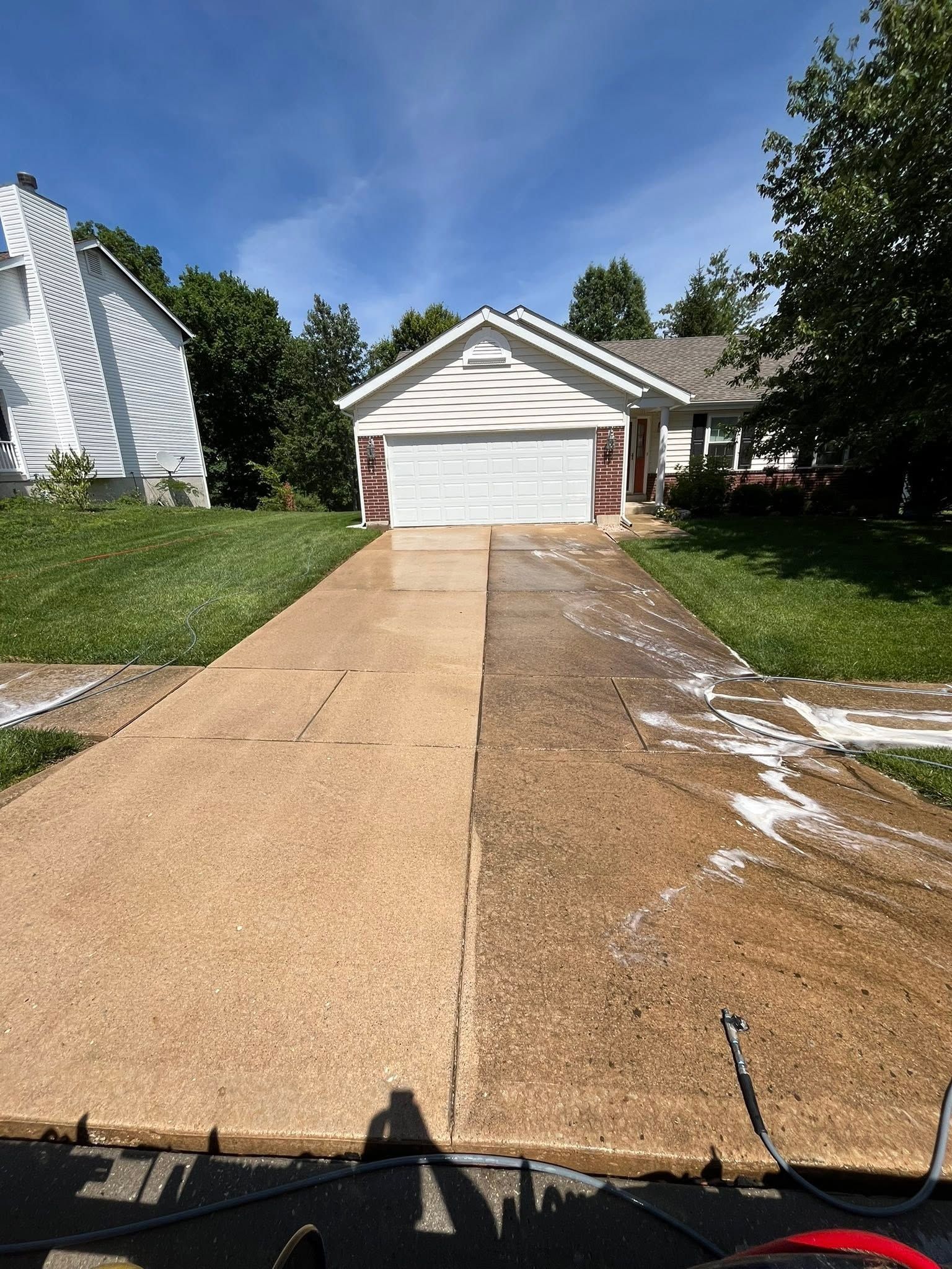 Driveway with a white garage, flanked by green lawns and trees on a sunny day.