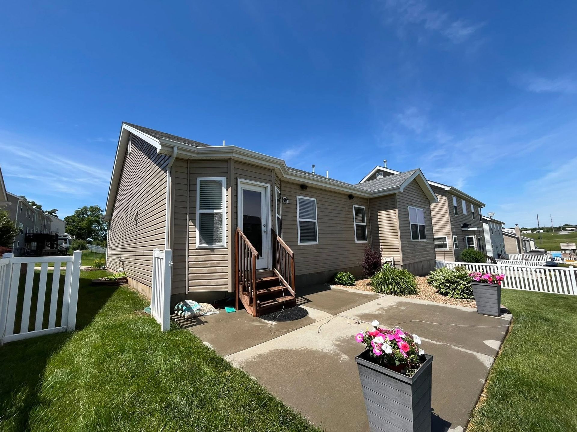 Suburban house exterior with small porch, flower planter, white fence, and blue sky