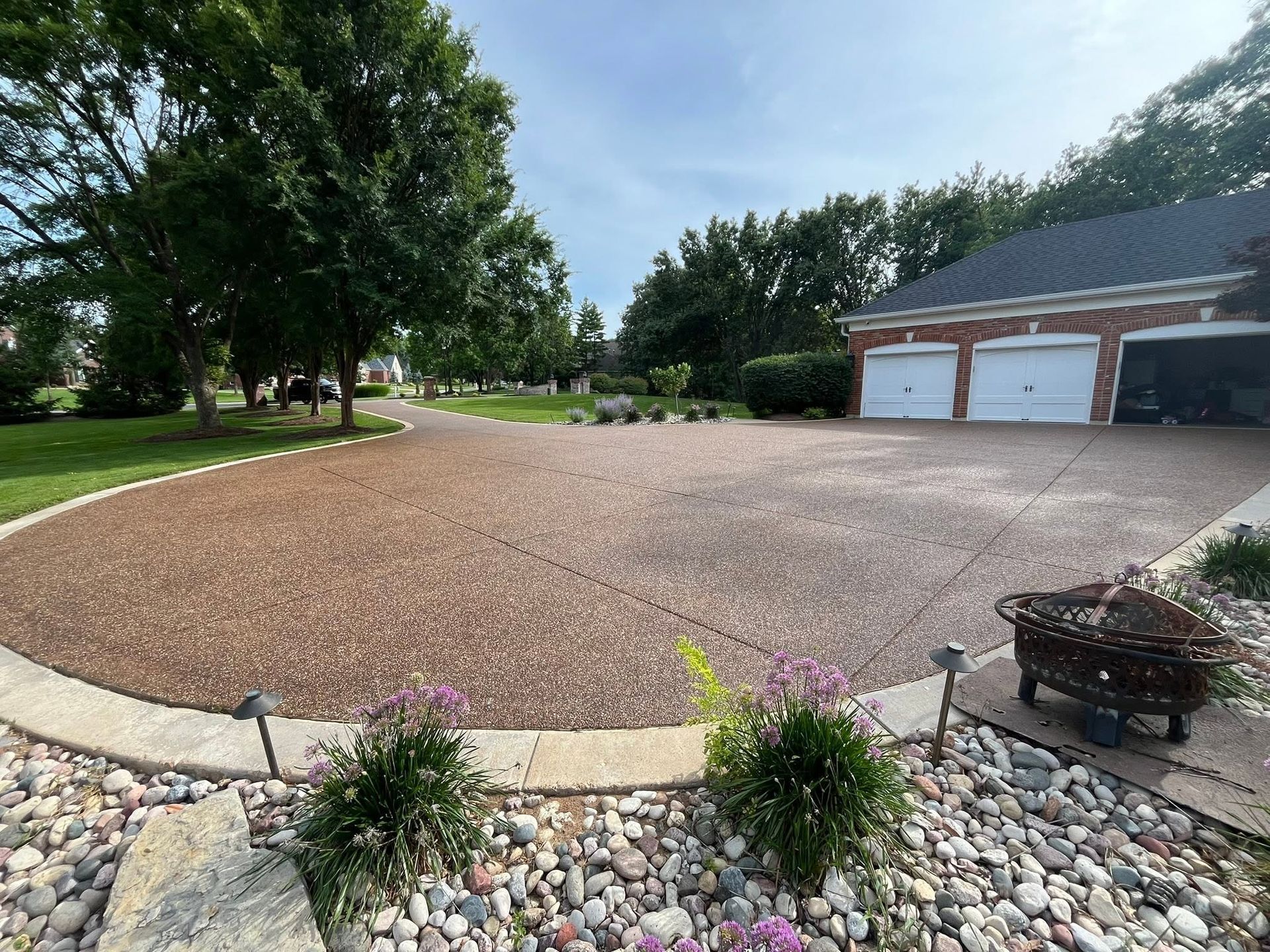 Curved gravel driveway beside a brick garage, bordered by stone landscaping and mature trees.