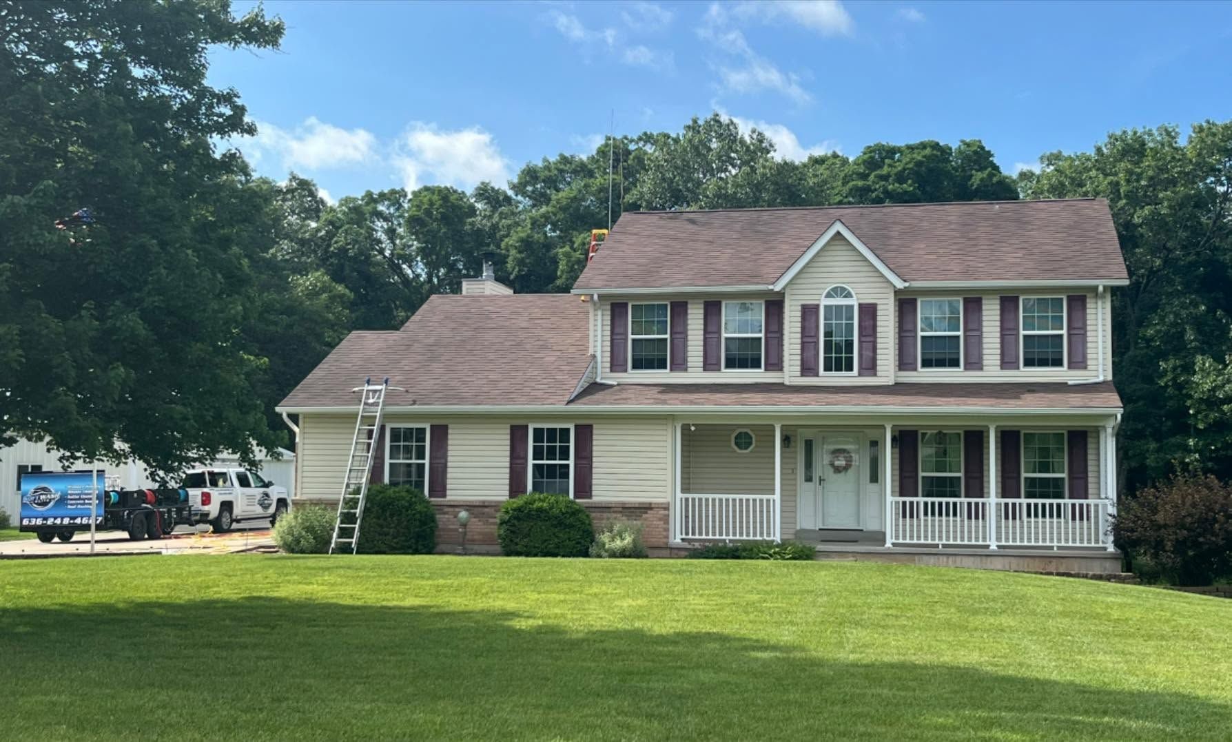 Suburban two-story house with white porch, gray siding, and green lawn under a blue sky