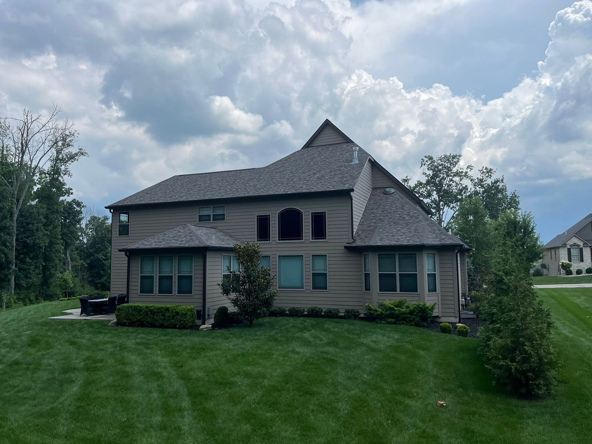 Suburban two-story house with gray siding, dark roof, and a green lawn under a cloudy sky