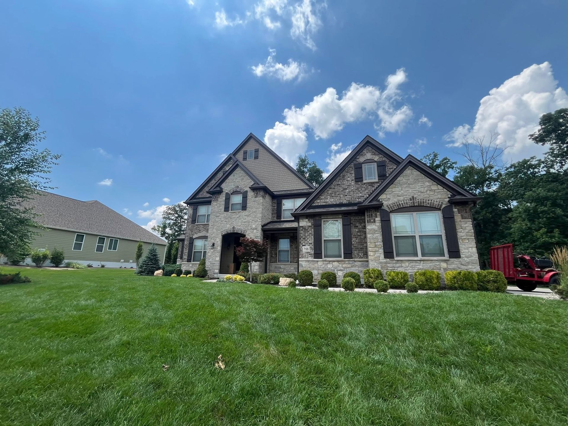 Suburban stone house with a manicured lawn under a bright blue sky with clouds