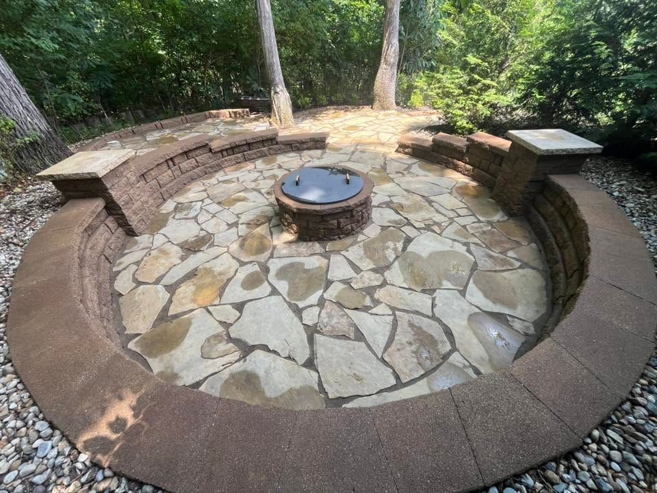 Stone fire pit with circular brick seating area in a wooded park setting
