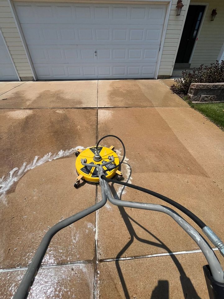 Yellow pressure washer cleaning a driveway, spraying water near a garage door.