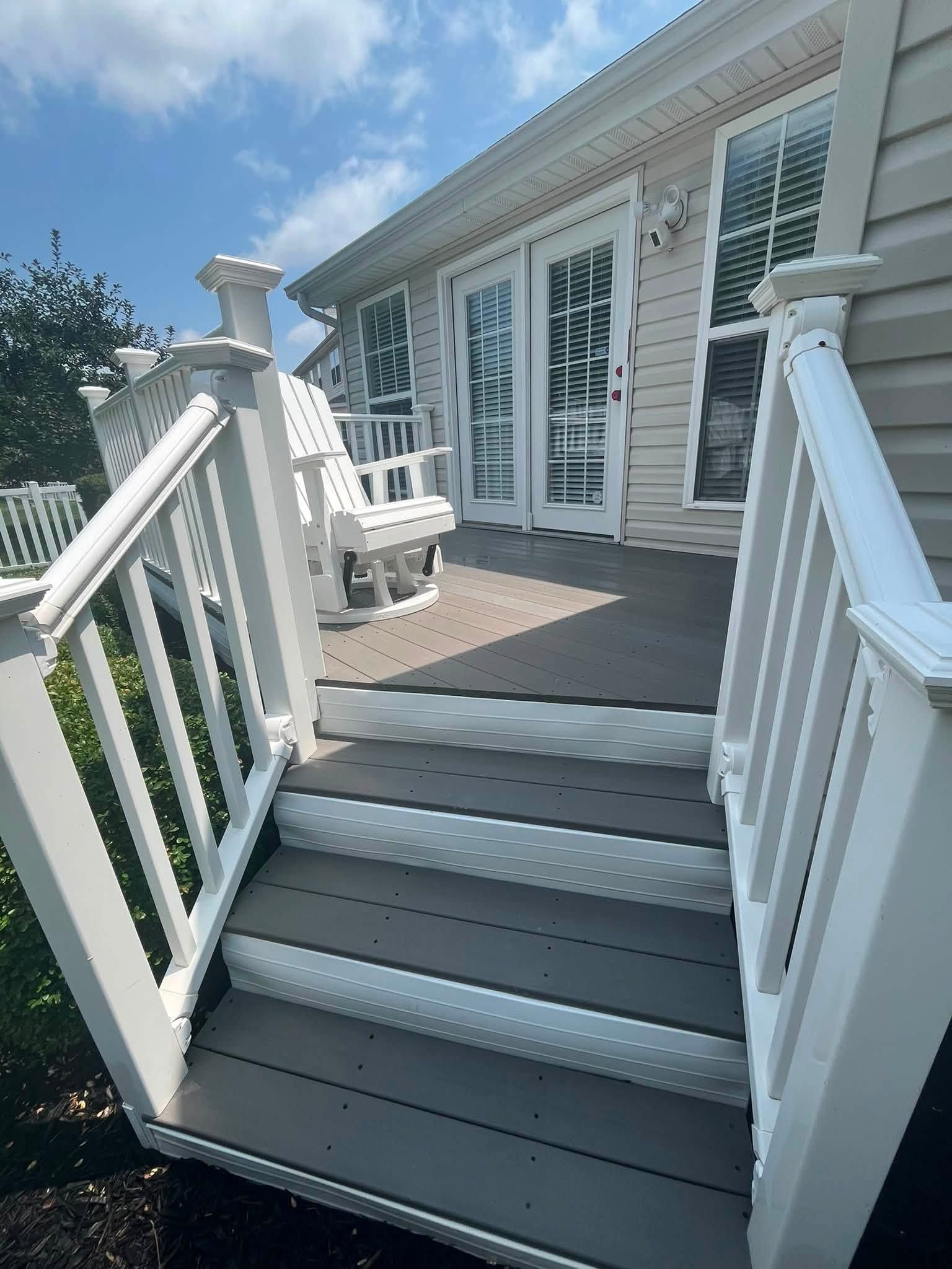 White front porch steps with railing leading to a gray deck outside a house.