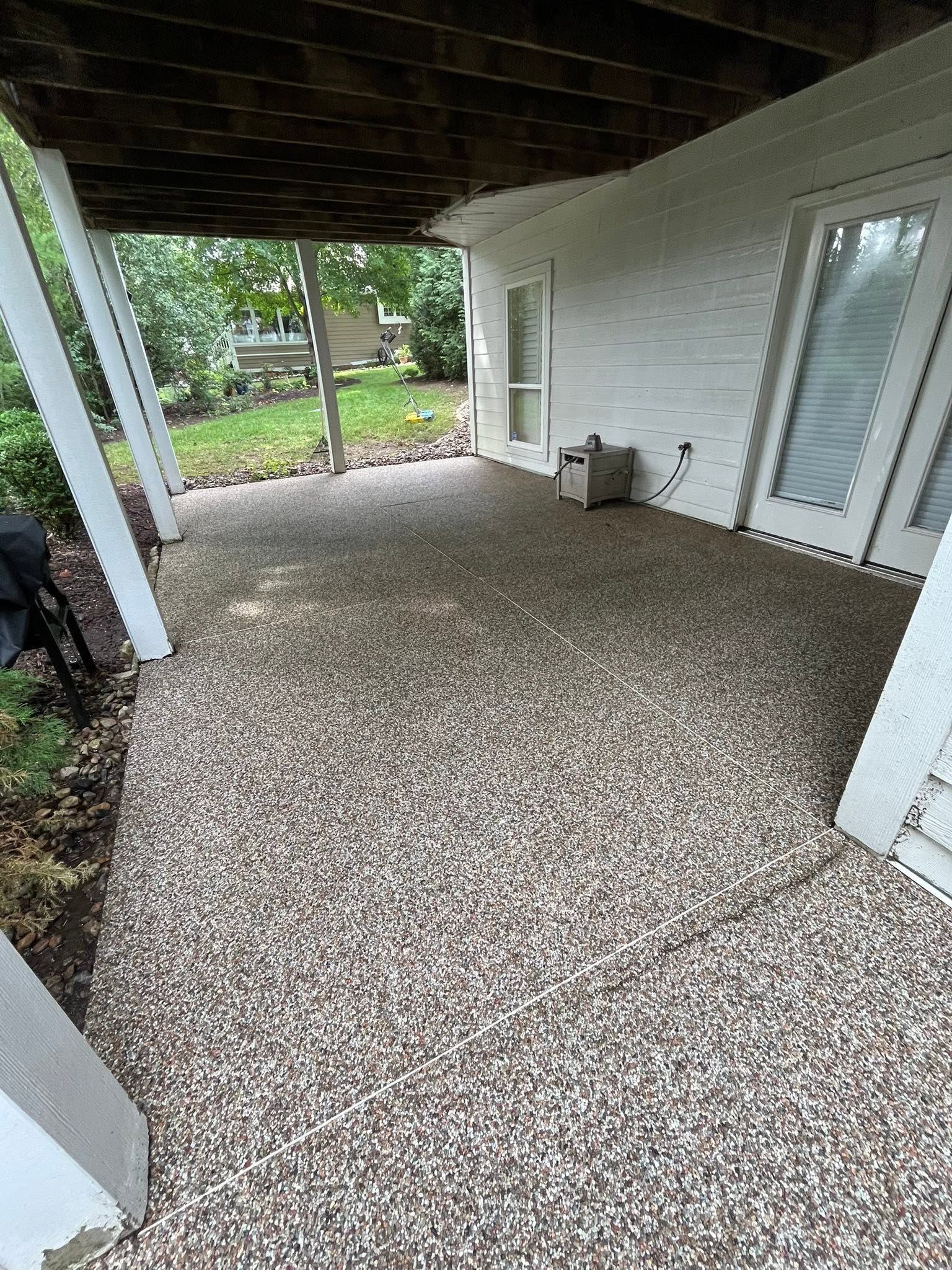 Covered patio with speckled concrete floor, white brick wall, and sliding glass doors opening to a backyard.