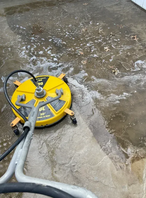 Yellow floor-cleaning machine on a wet concrete surface, scrubbing a soapy patio.