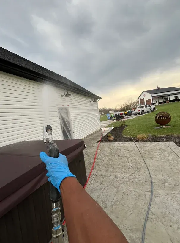 Blue-gloved hand holding a tool beside a house, with a cloudy sky and driveway in view