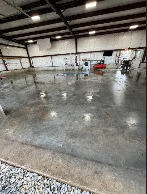 Empty warehouse with a freshly poured, wet concrete floor reflecting overhead lights and beams