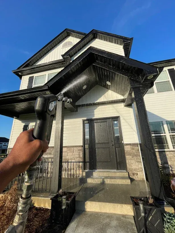 House exterior being washed with a pressure washer, with water spraying toward the front entrance.