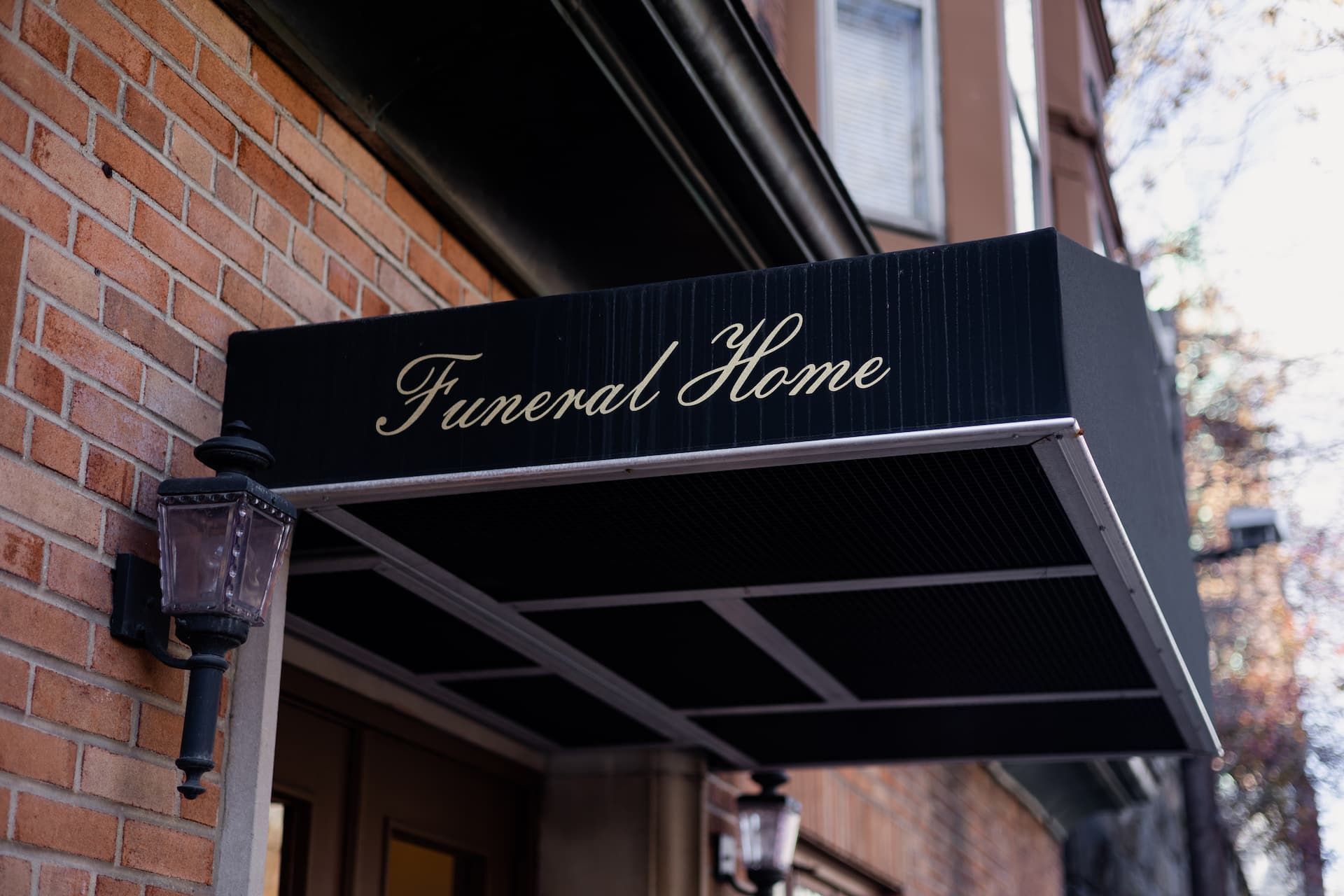 Funeral home entrance with black awning, gold lettering, brick building, and a lamp.