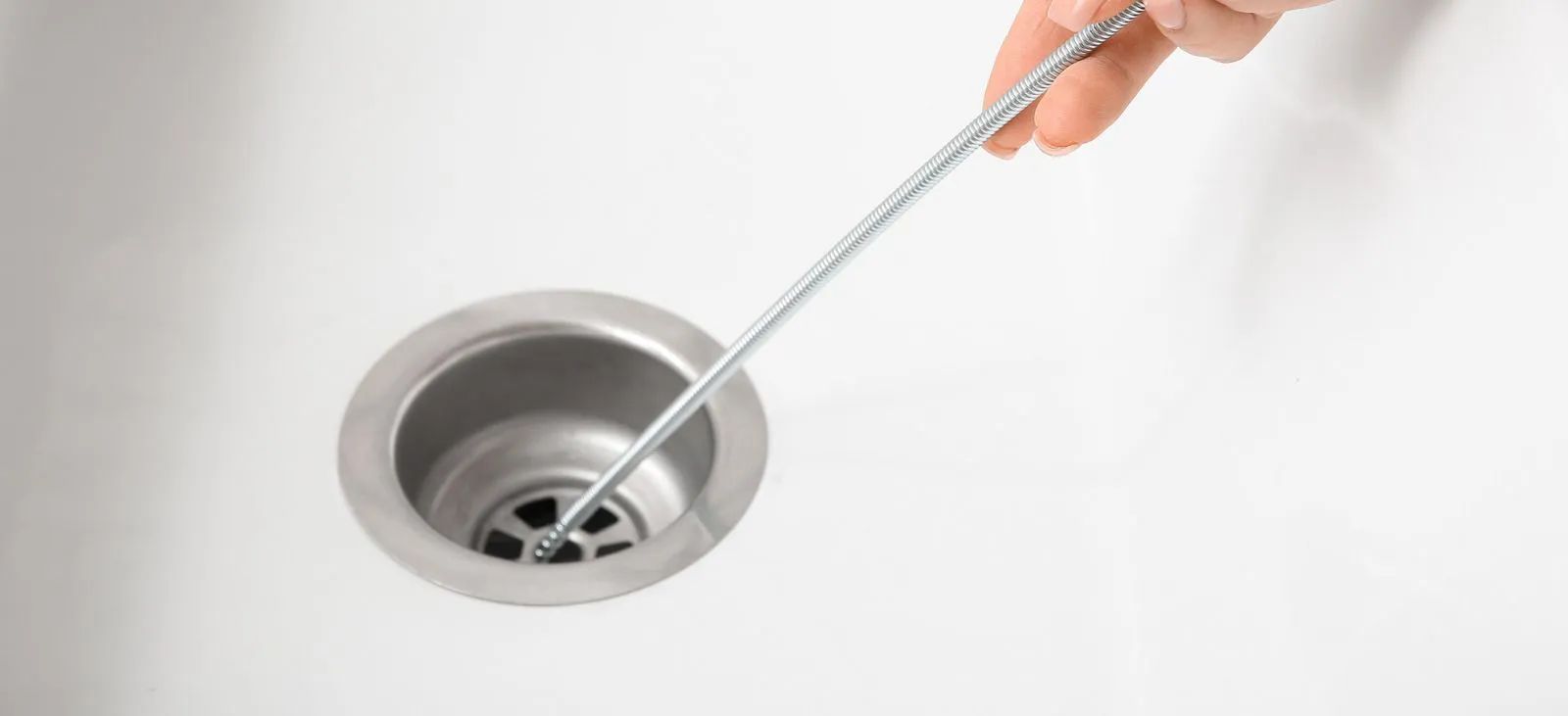 Hand using a drain cleaning tool in a silver sink drain