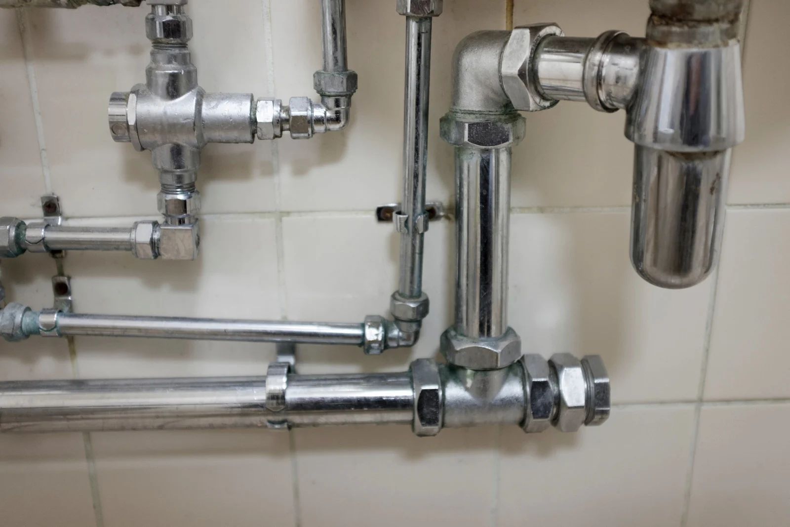 Shiny metal pipes and valves mounted on a white tiled wall in a utility area