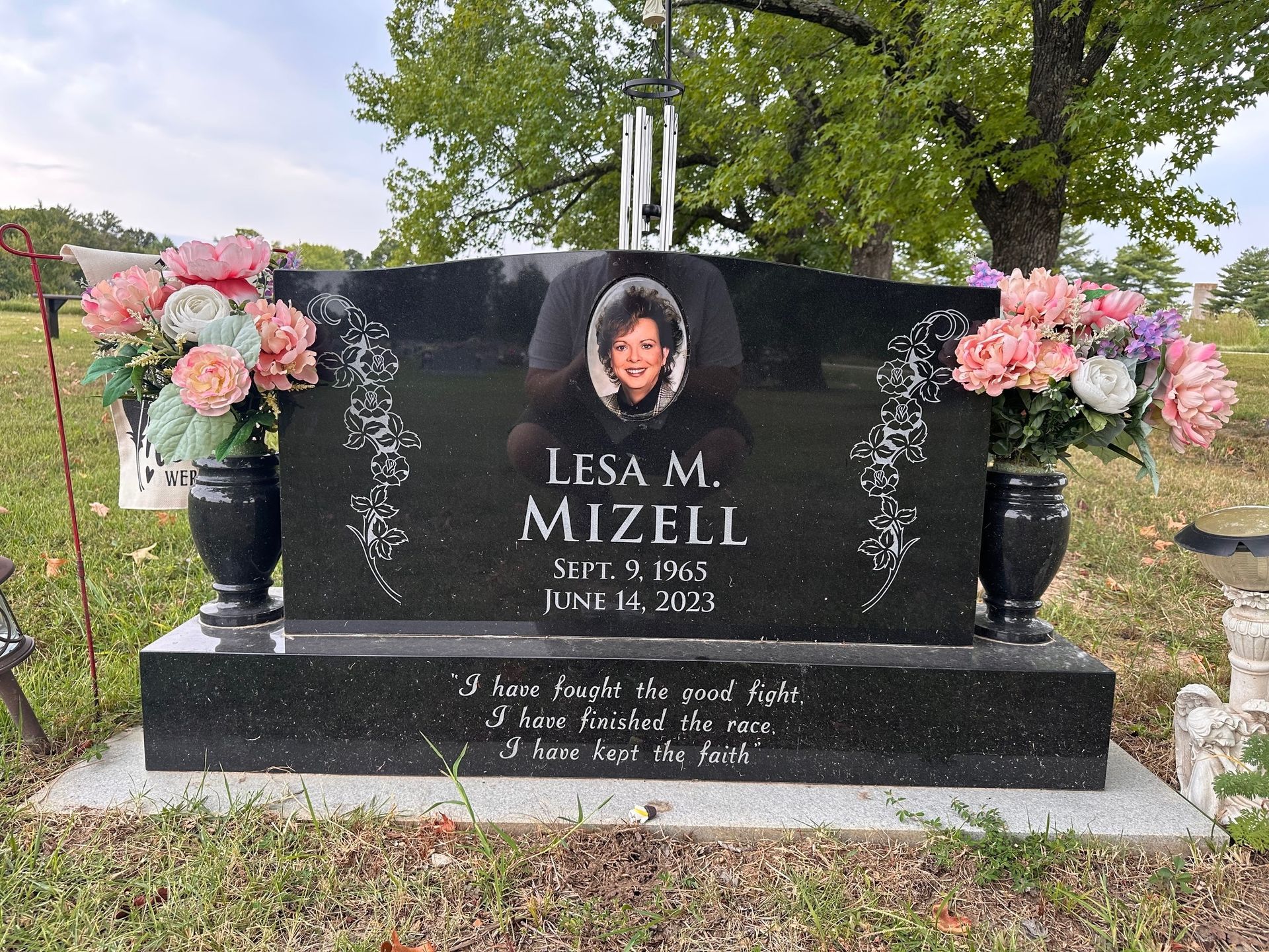 Black granite tombstone with a woman's photo, flowers, and inscription: