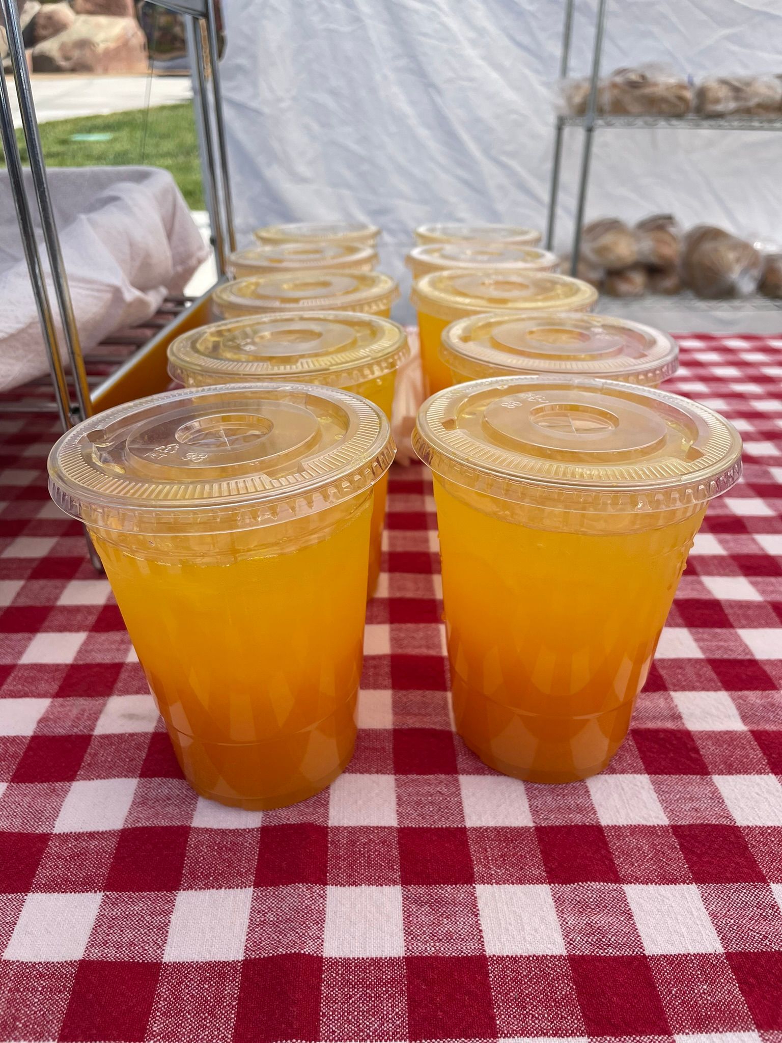 A row of cups of orange juice on a checkered table cloth.