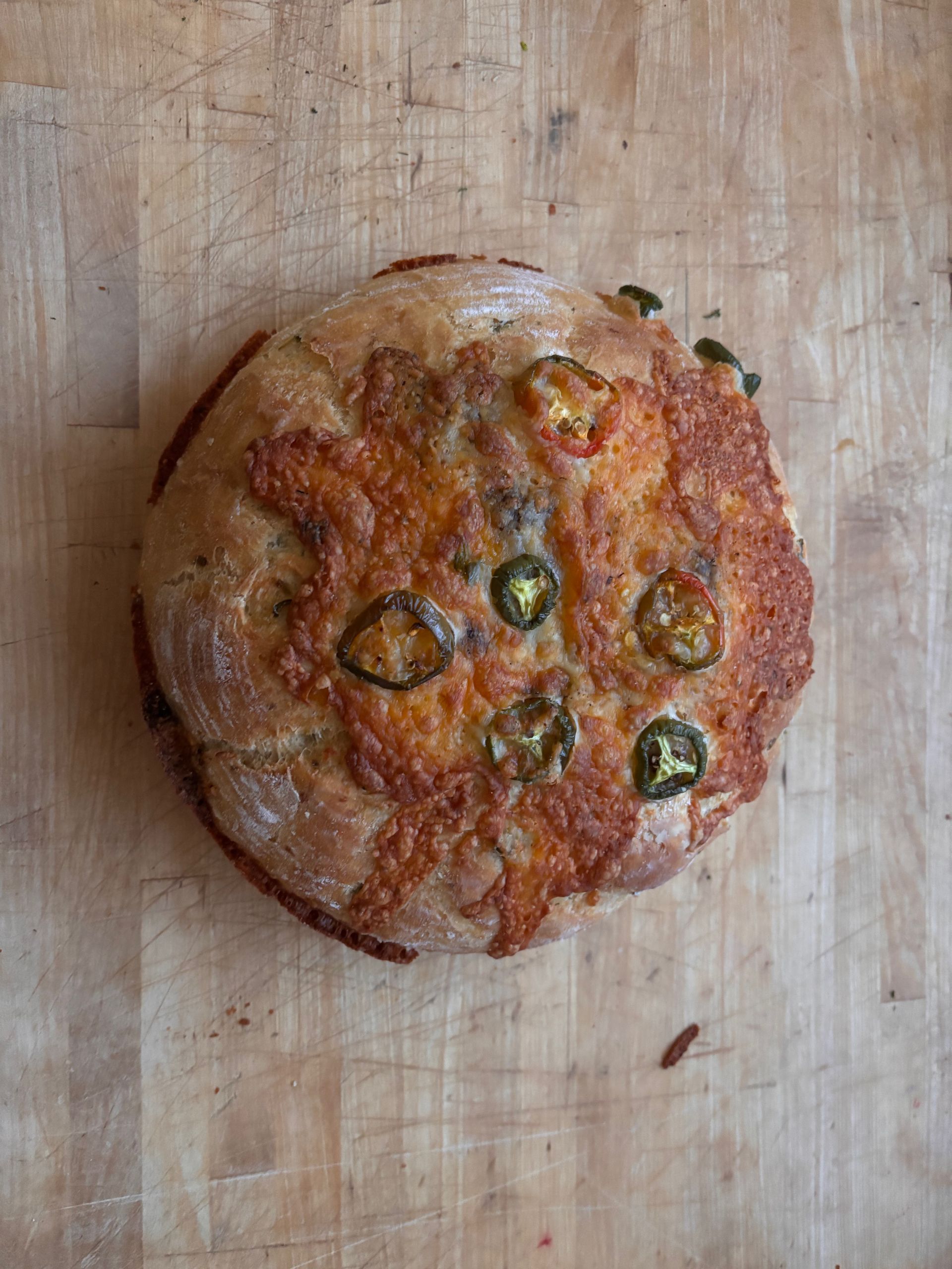 Round bread with melted cheese and jalapeño slices on a wooden surface.
