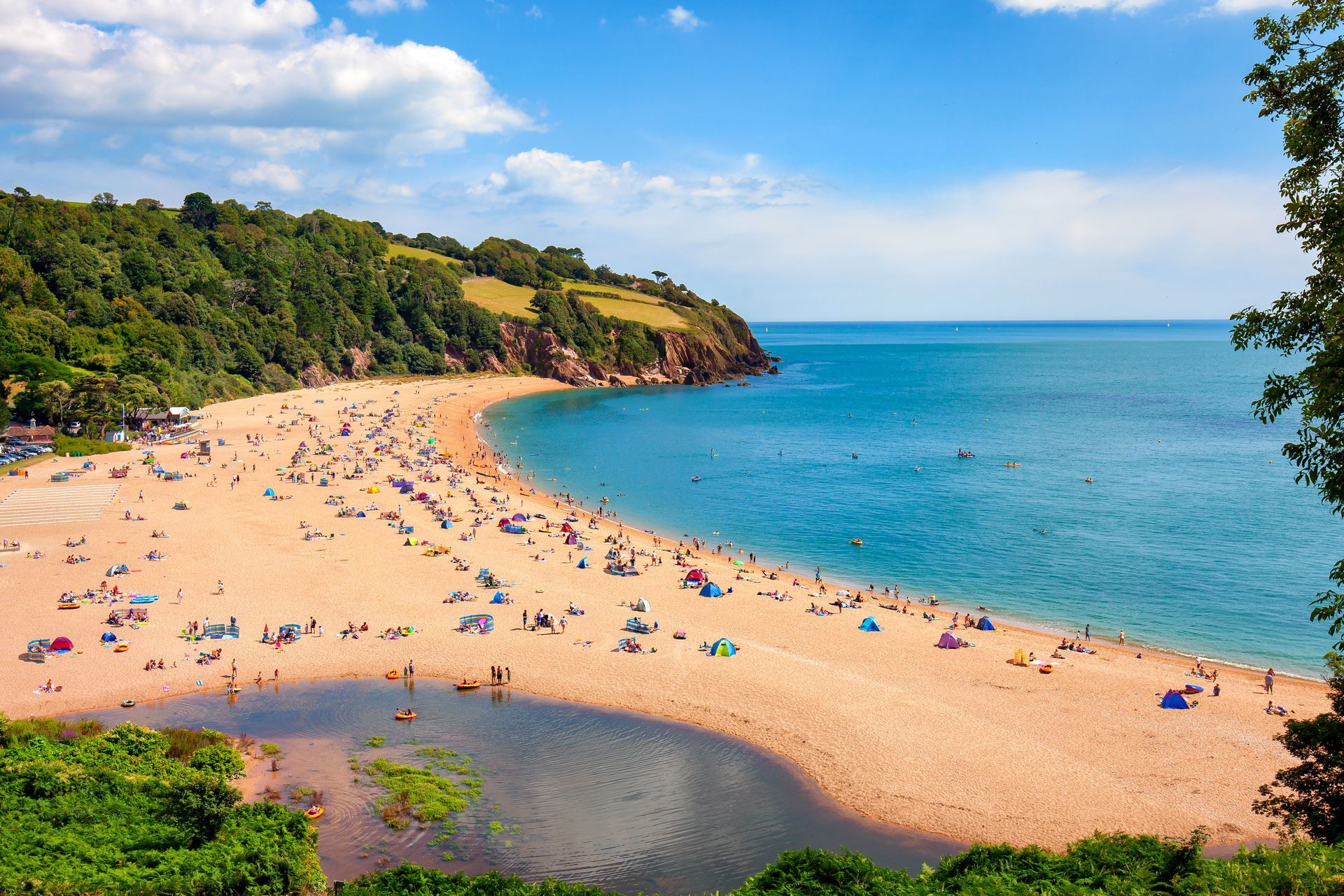 Sunny beach cove with turquoise water, sandy shore, and people lounging under colorful umbrellas