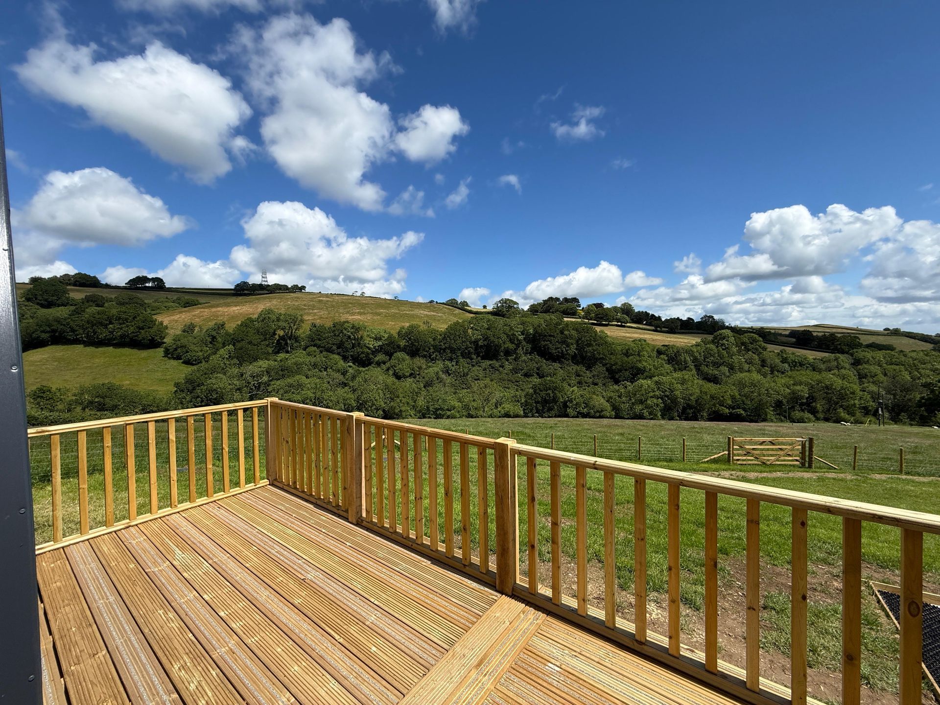 Wooden deck overlooking green hills under a blue sky with clouds